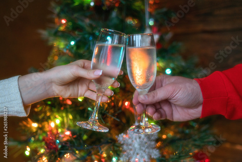 Cheers! Womam and man cheering with champagne flutes on the Christmas interior in the background. Holidays concept. Evening lights glowing. New Year celebration. Toned image. Selective focus.