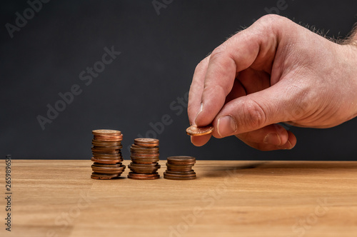 A hand stacking coins on a wooden table against a dark background.