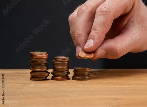 A hand stacking coins on a wooden table against a dark background.