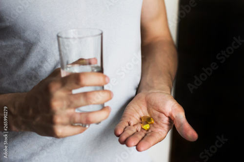  vitamins and a glass of water in the hands of a man