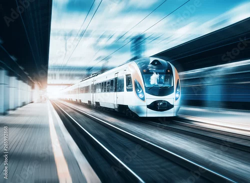 Obraz Wysoki prędkość pociąg przy stacją kolejową przy zmierzchem w Europa. Nowoczesny pociąg międzymiastowy na peronie kolejowym. Scena miejska z pięknym pociągiem pasażerskim na kolei i budynków. Krajobraz kolejowy