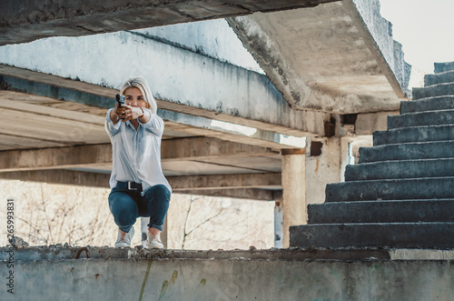 Woman in a white shirt squats on concrete steps, shoots a gun