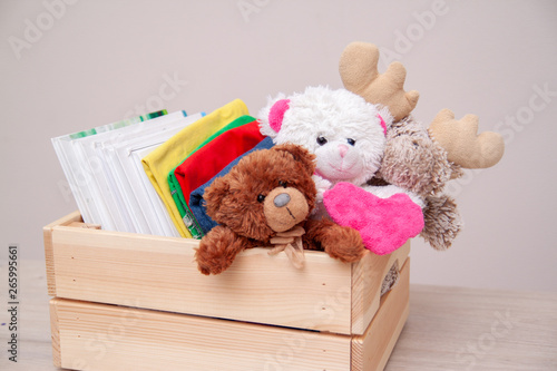 Donation concept. Donate box with kids clothes, books, school supplies and toys. Teddy bear with big pink heart in hands. Copyspace for text.