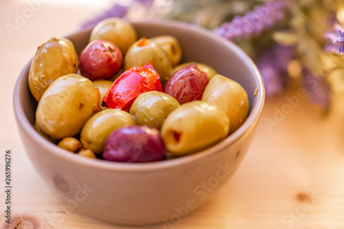 Olives stuffed with red pepper and herbs spices. Multi-colored olives in a small bowl on a wooden table. Lavender. Blurry background. Closeup. Soft focus. Copy space.