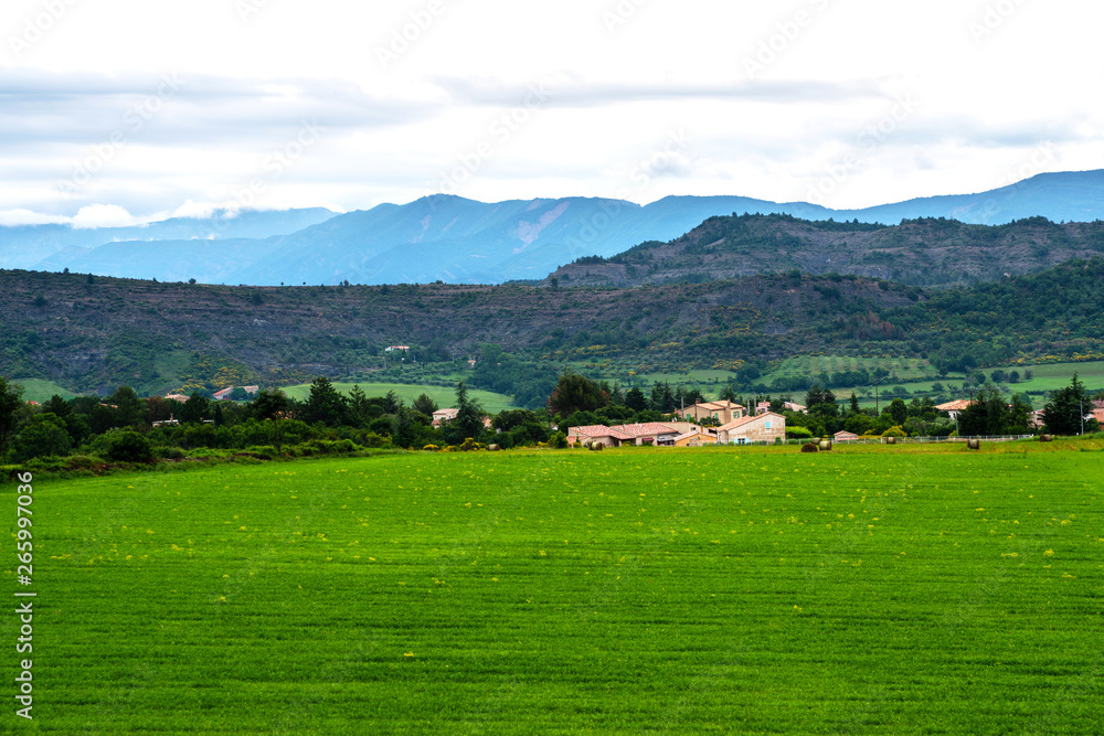 Picturesque rural landscape. Countryside of France with fresh green field, small village and mountain landscape in the background. Eco tourism.