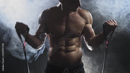 The concept of strength training. An athlete does resistance group exercises. Closeup bodybuilder body during workout with rubber band