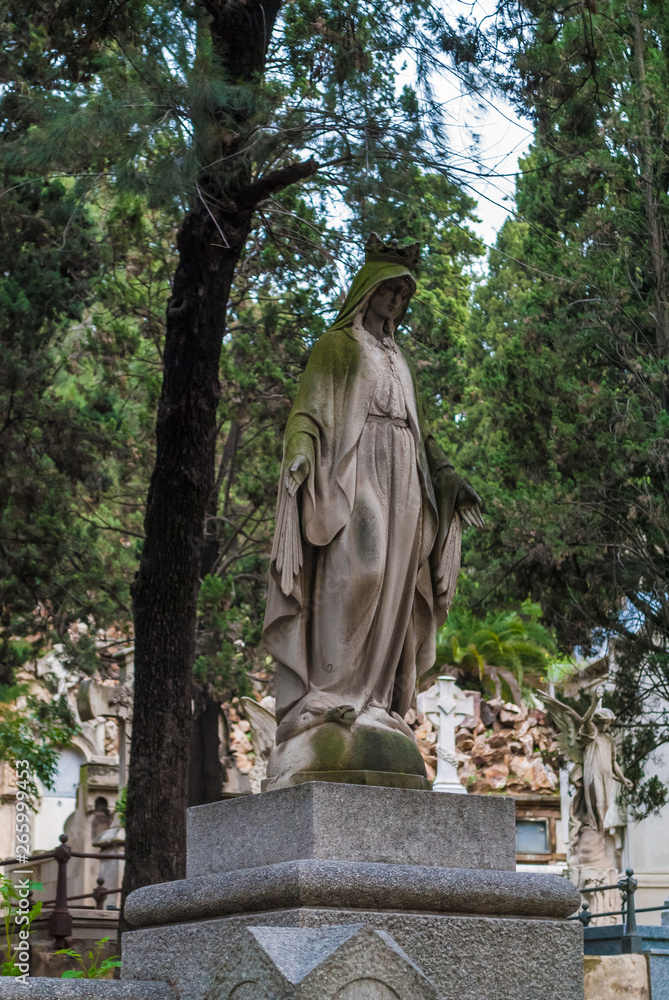 The sculpture of woman closeup on the background of graves and trees on the Montjuic Cemetery, Barcelona, Catalonia, Spain