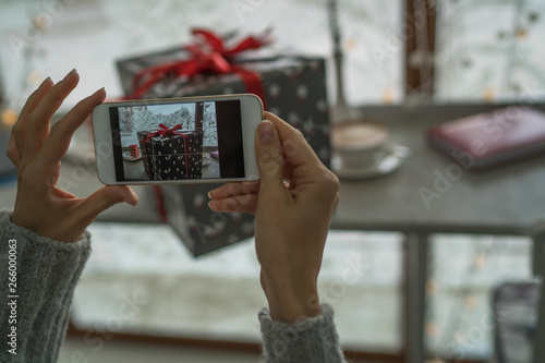 Young woman, blogger preparing for the Christmas holiday and making photo at smartphone. Woman's hands holding mobile phone and chatting online in social networks.Toned image. Selective focus.