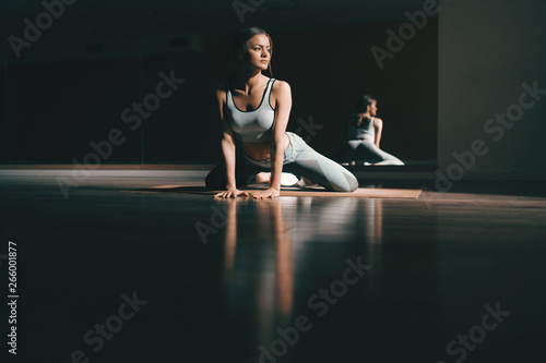 Young Caucasian brunette stretching on the mat in gym. In background mirror, night workout concept. You can have results or you can have excuses, you can't have both.