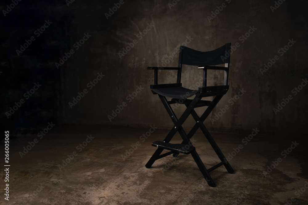 A black wooden chair stands in a photo studio against the background of an old, scratched concrete wall.