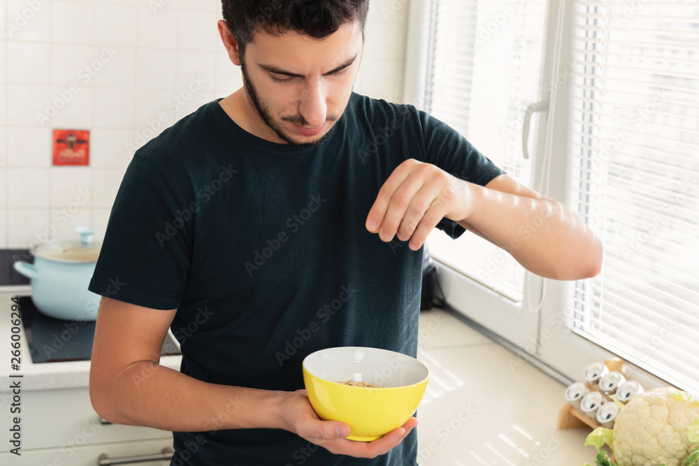 Young handsome man is having breakfast in the kitchen at home. The guy prepared himself oatmeal and a glass of milk for breakfast. Young handsome man is having breakfast in the kitchen at home. The guy prepared himself oatmeal and a glass of milk for breakfast.