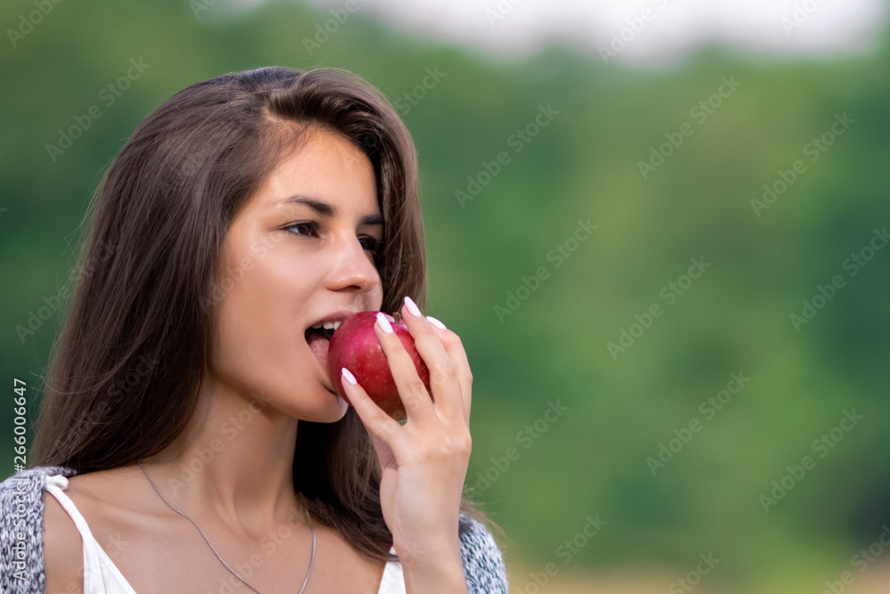 Young beautiful girl in white dress eating ripe organic apple. She is on the shore of the lake and enjoy a picnic and outdoor recreation. Young beautiful girl in white dress eating ripe organic apple. She is on the shore of the lake and enjoy a picnic and outdoor recreation.