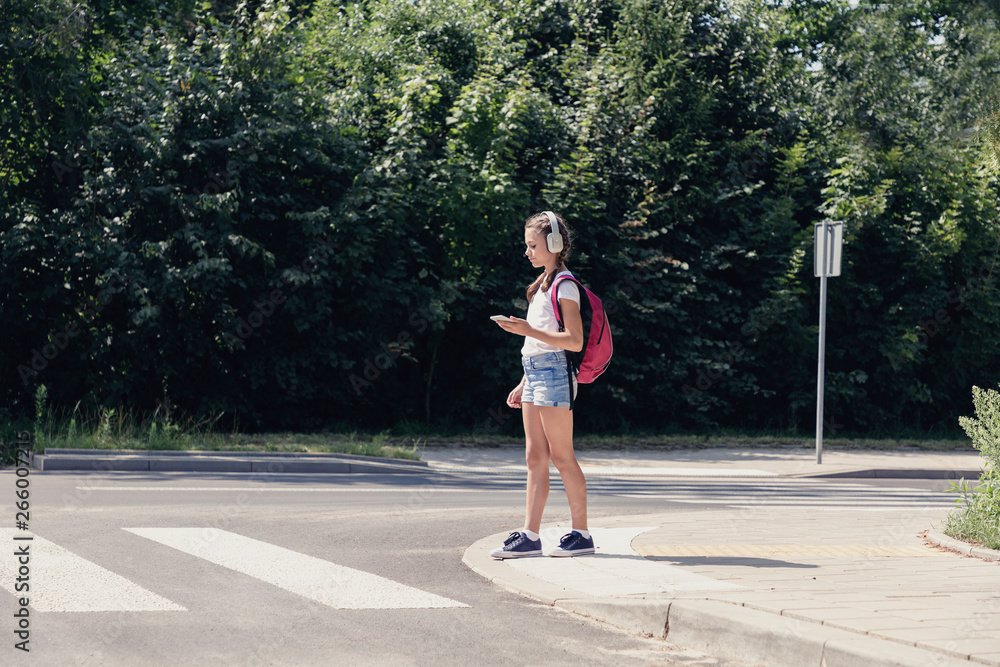 Pretty teenage schoolgirl with headphones and mobile phone on pedestrian crossing Pretty teenage schoolgirl with headphones and mobile phone on pedestrian crossing