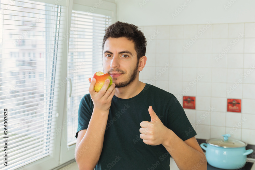 Fototapeta premium A young man eats a ripe organic apple. Enjoys a healthy lifestyle.