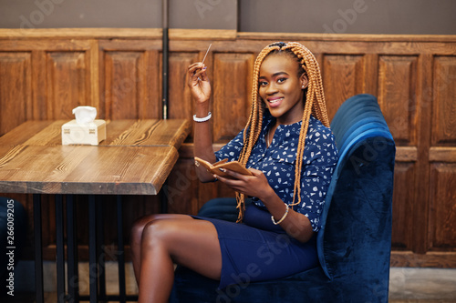 Portrait of beautiful young african business woman, wear on blue blouse and skirt, sitting at restaurant and hold credit card in hand.
