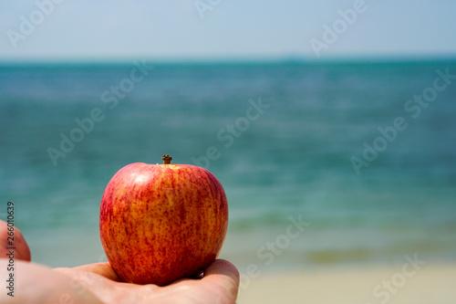 Red ripe Apple in the palm of your hand on the beach.Views of the blue sea
