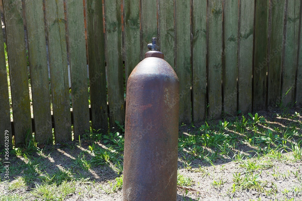 brown old metal gas cylinder dug into the ground in the green grass near the fence outside brown old metal gas cylinder dug into the ground in the green grass near the fence outside