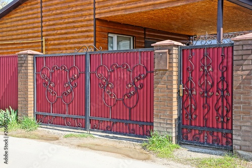 red metal gate with a black forged pattern on the street near the asphalt road