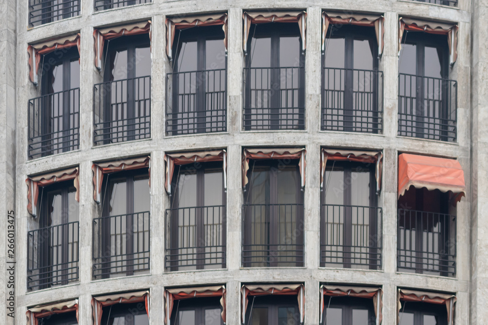 Fototapeta premium Altbaufassade mit kleinen roten Markisen, von denen eine einzige ausgefahren ist