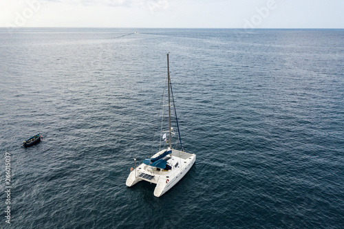 Landscape. Quiet, windless weather. White sailing catamaran is anchored close to the shore of the ocean. The view from the top. Copy space.
