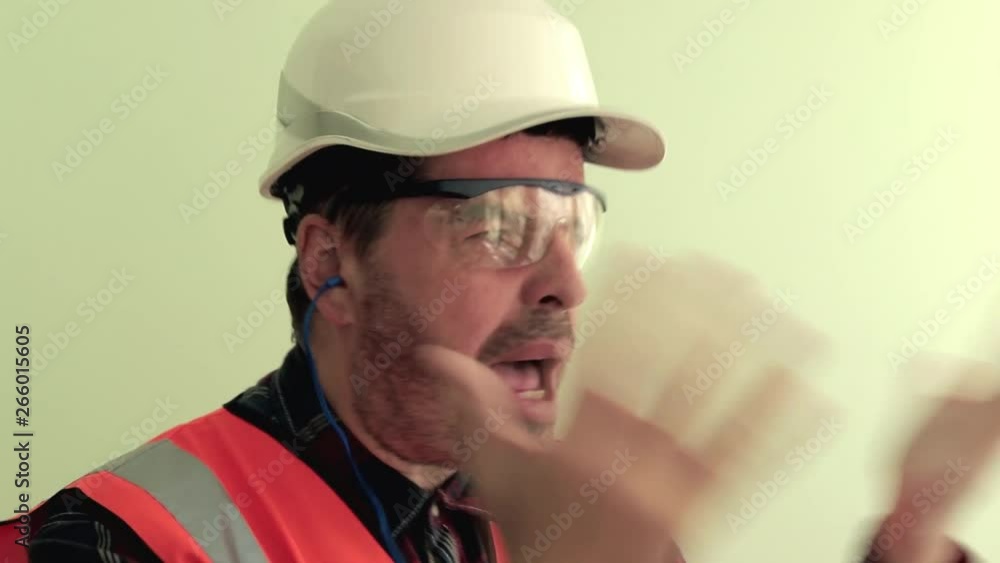 Caucasian unshaven man worker dressed in a reflective vest, protective glasses and white helmet nervously arguing, shouting, waving his arms Isolated on light green background. Caucasian unshaven man worker dressed in a reflective vest, protective glasses and white helmet nervously arguing, shouting, waving his arms Isolated on light green background.