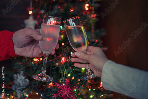 Two glasses of champagne raised in a toast against a Christmas tree glowing lights. Holiday and togetherness a family Christmas and Happy New Year. Party time. Couple with champagne. Selective focus.