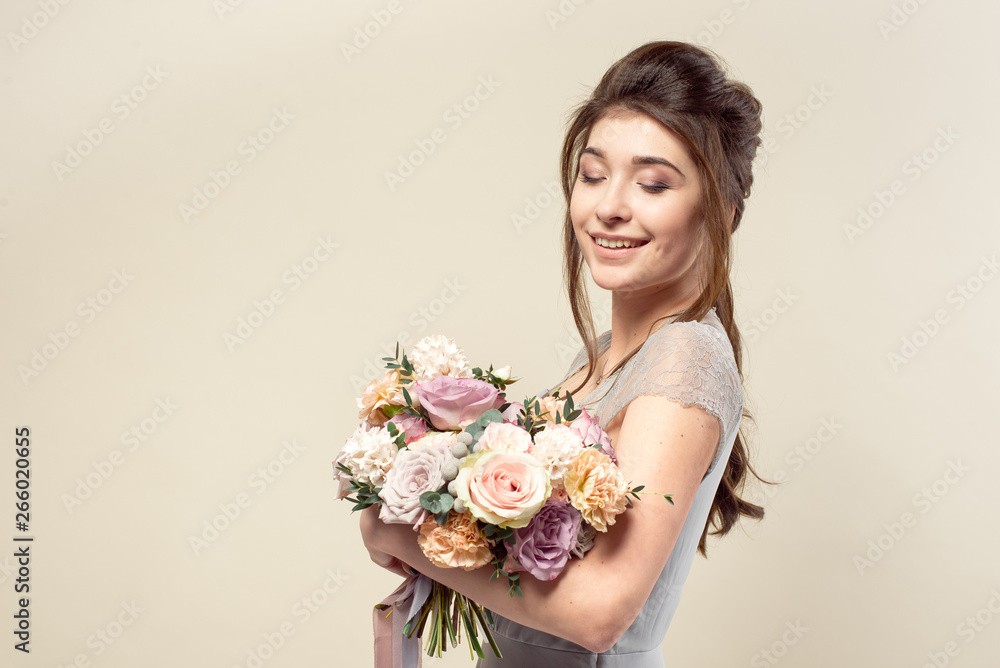 Elegant girl with a haircut in a soft blue dress and make-up is holding a bouquet of a stylish bouquet of flowers.