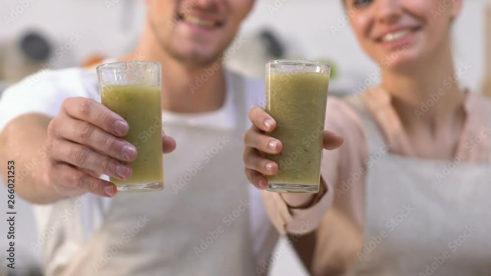 Healthy family couple showing glasses with green smoothies at camera, diet Healthy family couple showing glasses with green smoothies at camera, diet