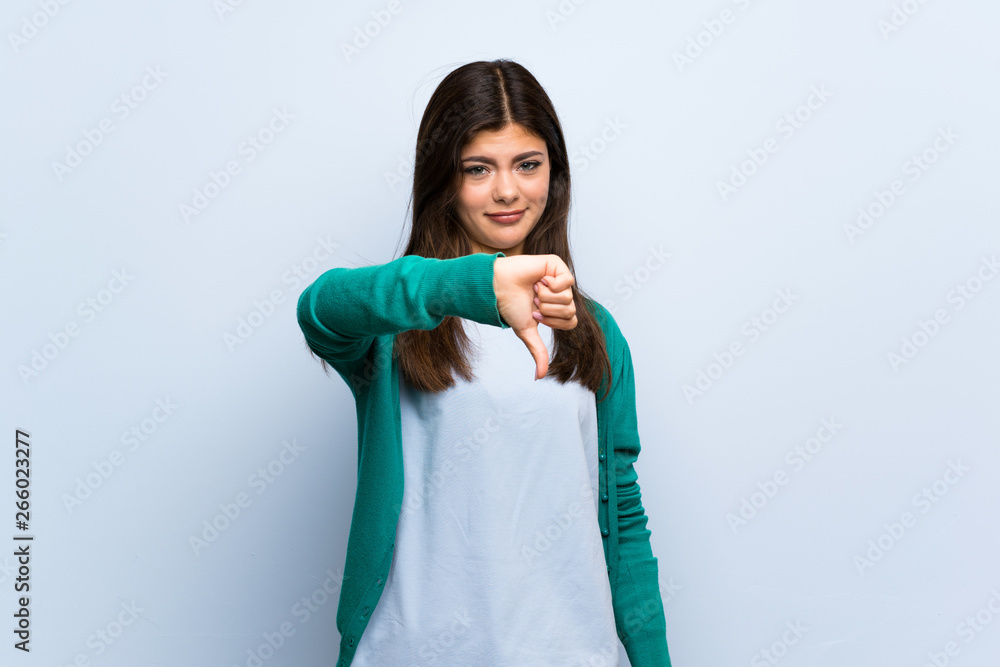 Teenager girl over blue wall showing thumb down with negative expression Teenager girl over blue wall showing thumb down with negative expression