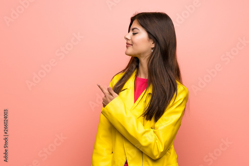 Teenager girl over pink wall pointing back