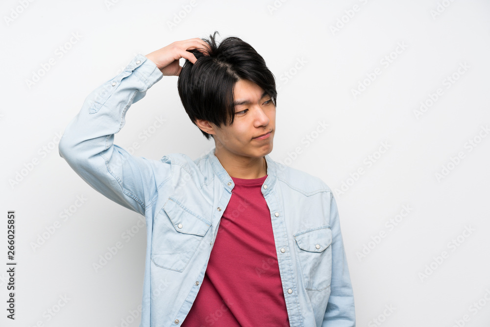 Asian man on isolated white background having doubts while scratching head Asian man on isolated white background having doubts while scratching head