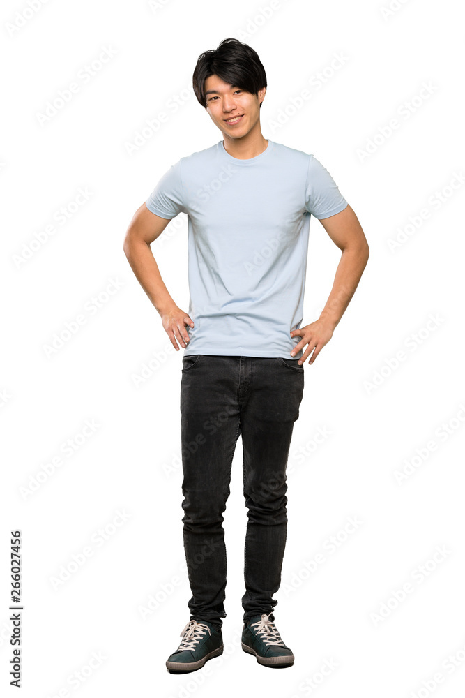A full-length shot of a Asian man with blue shirt posing with arms at hip and smiling over isolated white background A full-length shot of a Asian man with blue shirt posing with arms at hip and smiling over isolated white background