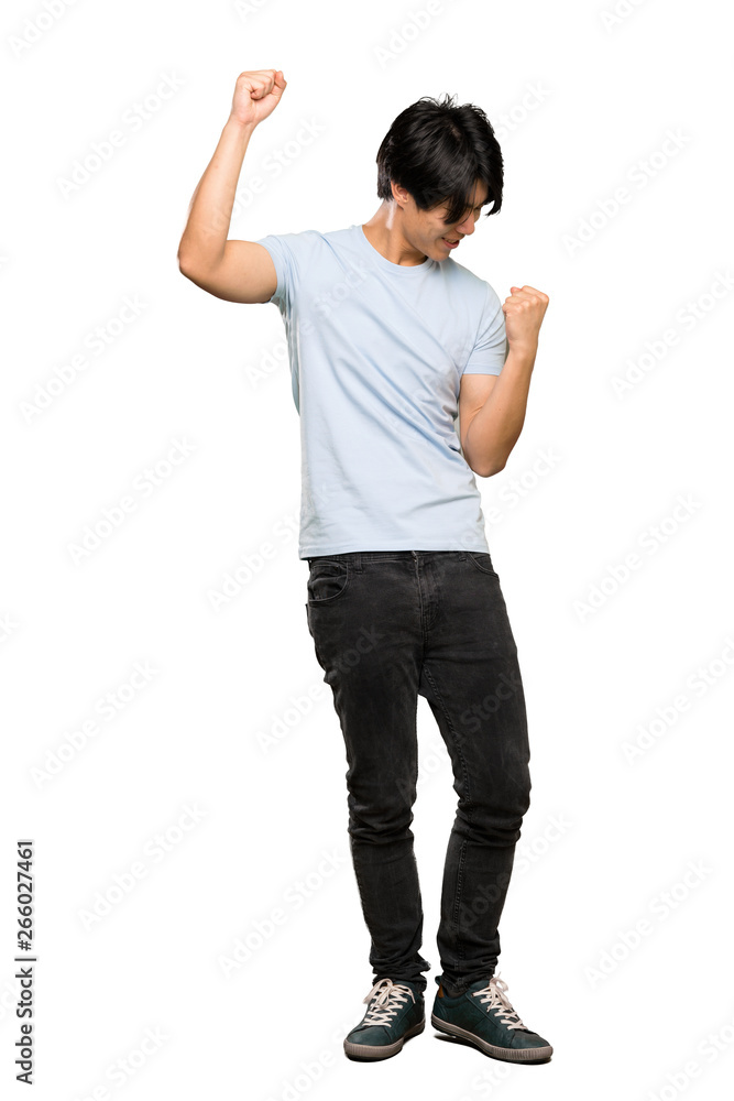 A full-length shot of a Asian man with blue shirt celebrating a victory over isolated white background - obrazy, fototapety, plakaty 
