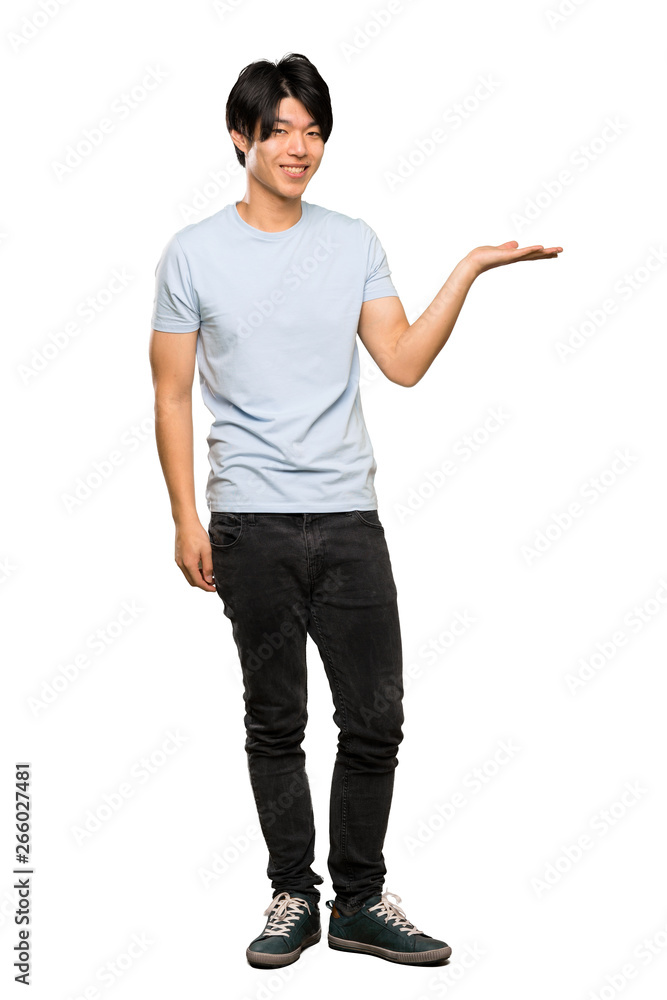 A full-length shot of a Asian man with blue shirt holding copyspace imaginary on the palm to insert an ad over isolated white background A full-length shot of a Asian man with blue shirt holding copyspace imaginary on the palm to insert an ad over isolated white background