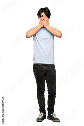 A full-length shot of a Asian man with blue shirt covering mouth with hands over isolated white background