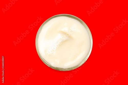 Spa cream in a glass cup placed on a red background. Cosmetic cream camomile. Organic cosmetics with coconut on red background top view.