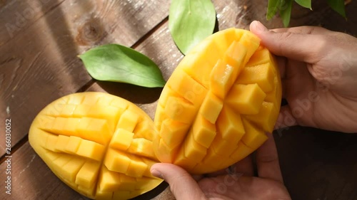 Person opens cut mango over wooden table background, closeup view. Healthy food, juicy tropical fruit