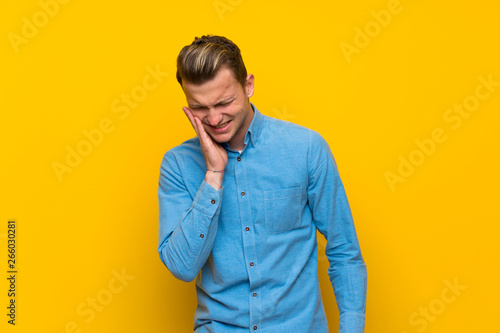 Blonde man over isolated yellow wall with toothache