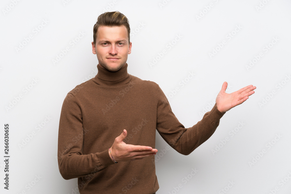 Blonde man over isolated white wall extending hands to the side for inviting to come Blonde man over isolated white wall extending hands to the side for inviting to come