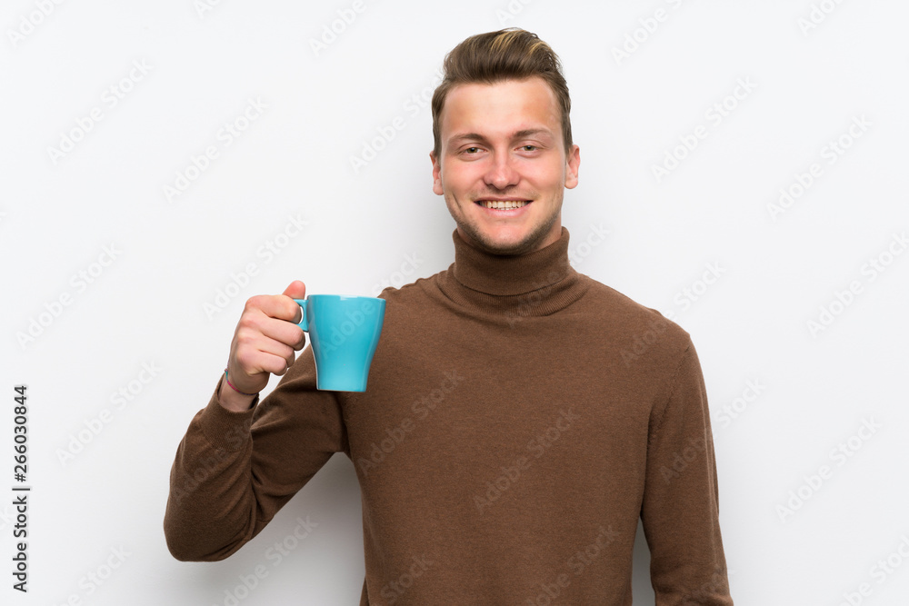 Blonde man over isolated white wall holding a hot cup of coffee