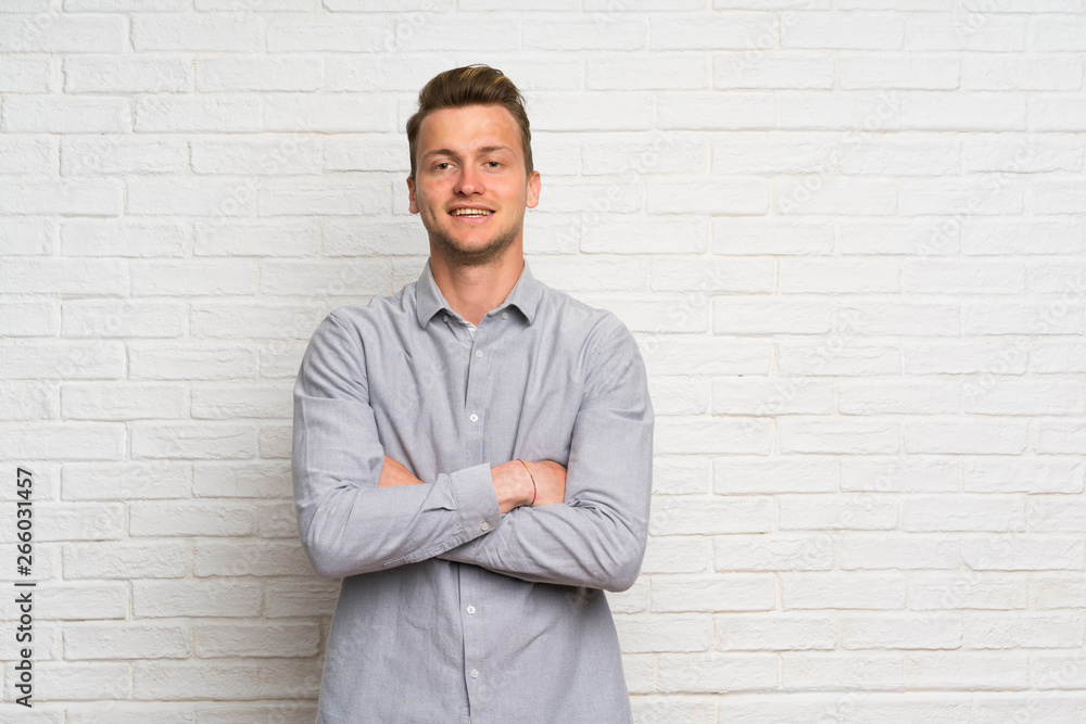 Blonde man over white brick wall keeping the arms crossed in frontal position Blonde man over white brick wall keeping the arms crossed in frontal position