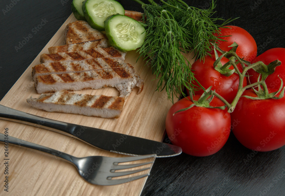 Greens with tomatoes and grilled Turkey steak on a chopping Board. Cutlery on a cutting Board. Top view Greens with tomatoes and grilled Turkey steak on a chopping Board. Cutlery on a cutting Board. Top view