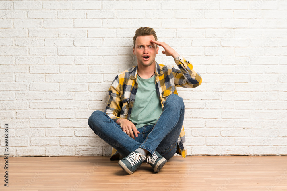 Blonde man sitting on the floor has just realized something and has intending the solution Blonde man sitting on the floor has just realized something and has intending the solution