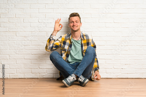 Blonde man sitting on the floor showing ok sign with fingers