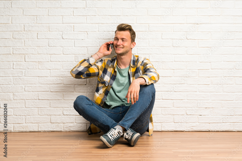 Blonde man sitting on the floor keeping a conversation with the mobile phone Blonde man sitting on the floor keeping a conversation with the mobile phone
