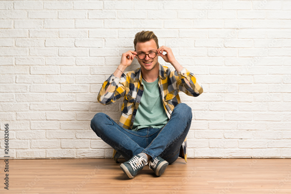 Blonde man sitting on the floor with glasses and surprised Blonde man sitting on the floor with glasses and surprised