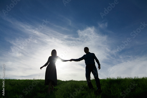 silhouettes of love couples on the nature summer evening.young man and woman tenderly embracing in the sunset.Loving couple hold hands walking on a green field.concept love story.