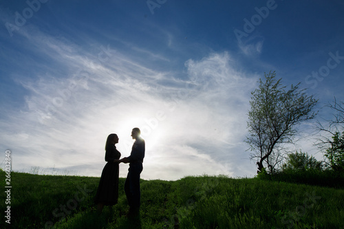 silhouettes of couple in love on nature in summer evening. young man and woman tenderly embracing in the sunset. Lovers hold hands walking on a green field. concept love story outdoors