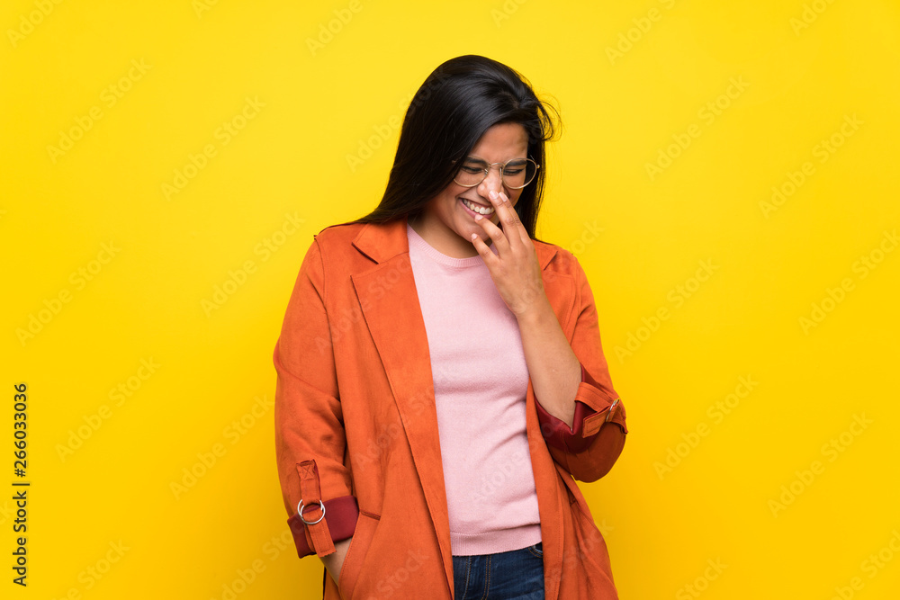 Young Colombian girl over yellow wall posing with arms at hip and laughing Young Colombian girl over yellow wall posing with arms at hip and laughing
