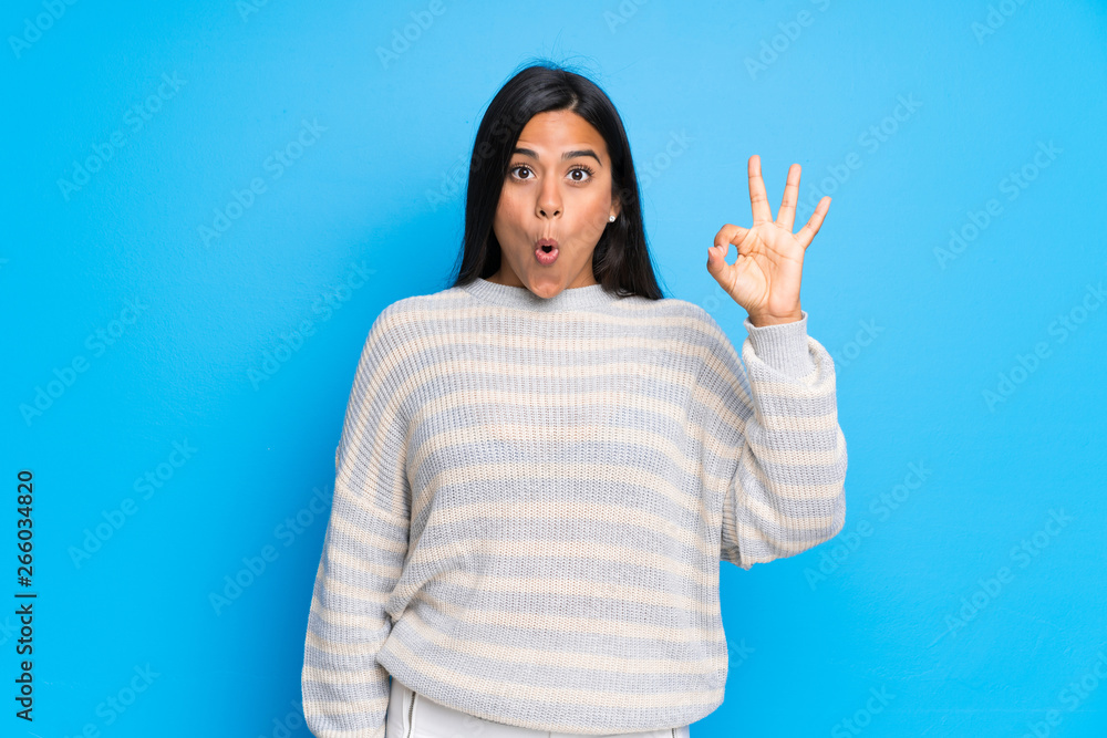 Young Colombian girl with sweater surprised and showing ok sign Young Colombian girl with sweater surprised and showing ok sign